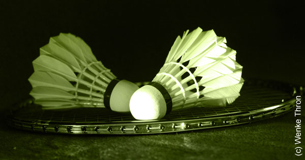 Hier wird ein Foto angezeigt auf dem zwei Federbälle zu sehen  sind, die auf einem Badmintonschläger liegen.